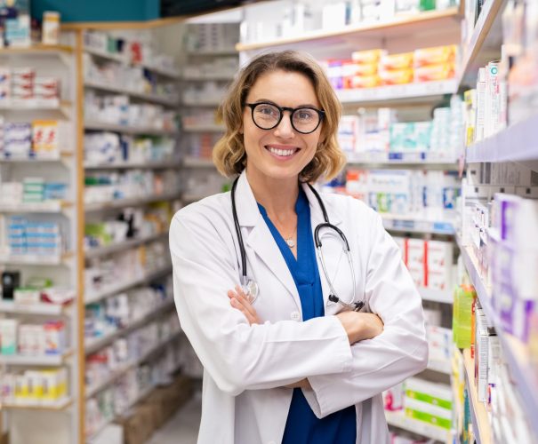 Happy smiling pharmacist in drugstore Portrait of mature woman pharmacist at pharmacy wearing labcoat with stethoscope. Happy smiling doctor standing in modern pharmacy drugstore. Friendly young pharmacist owner standing in shop and looking at camera.